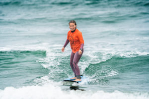 Image of program particpant standing on surf board and riding a wave