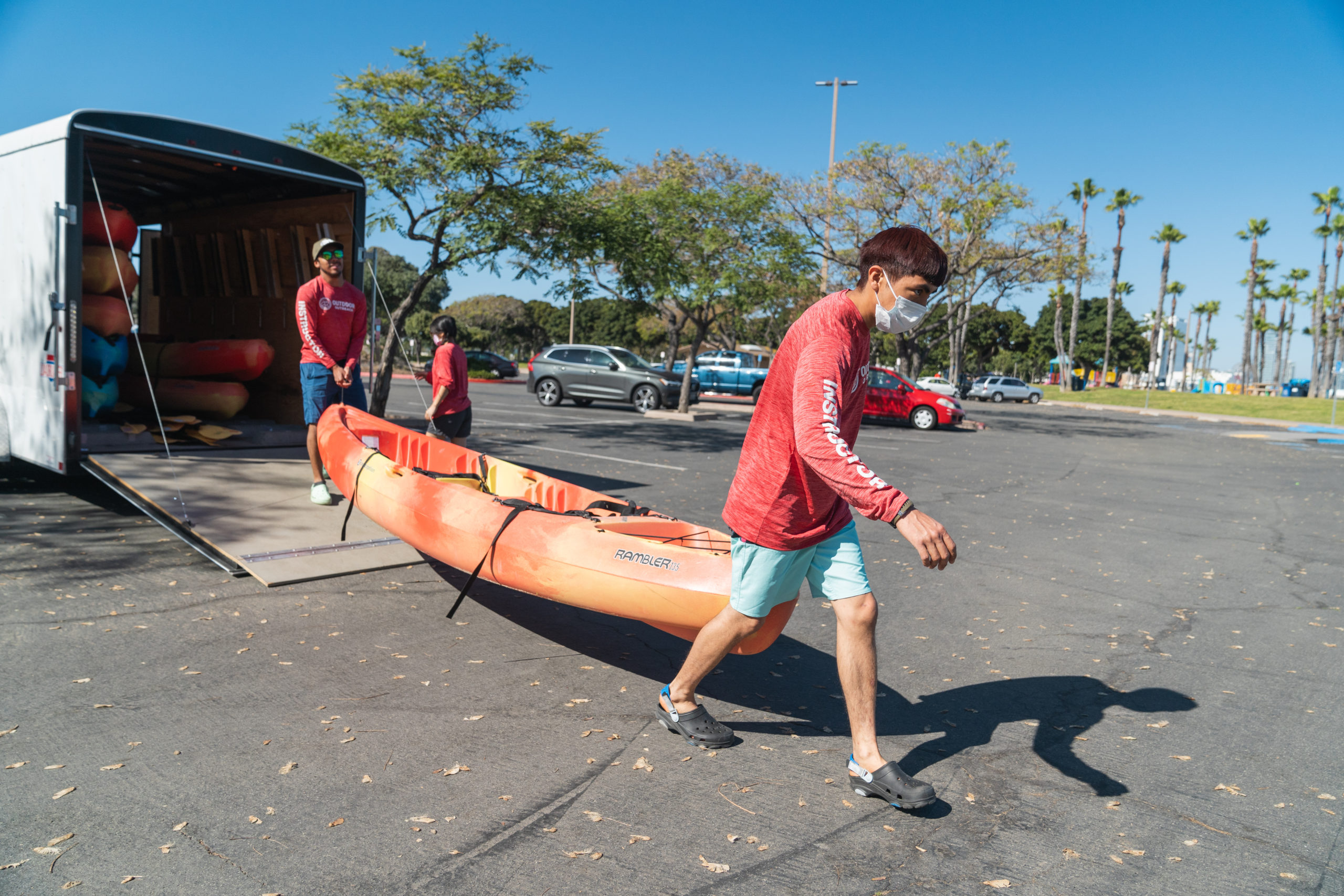 Two Outdoor Outreach instructors unloading kayaks from a trailer in the parking lot of Tidelands Park. 