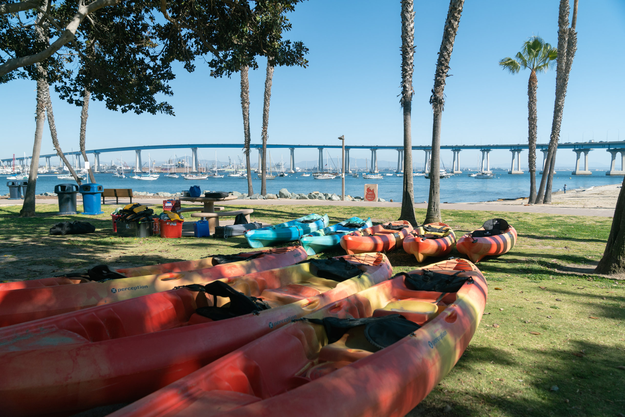 Blue and orange kayaks laid out on the grass at Tidelands Park facing the bay and Coronado Bridge. 