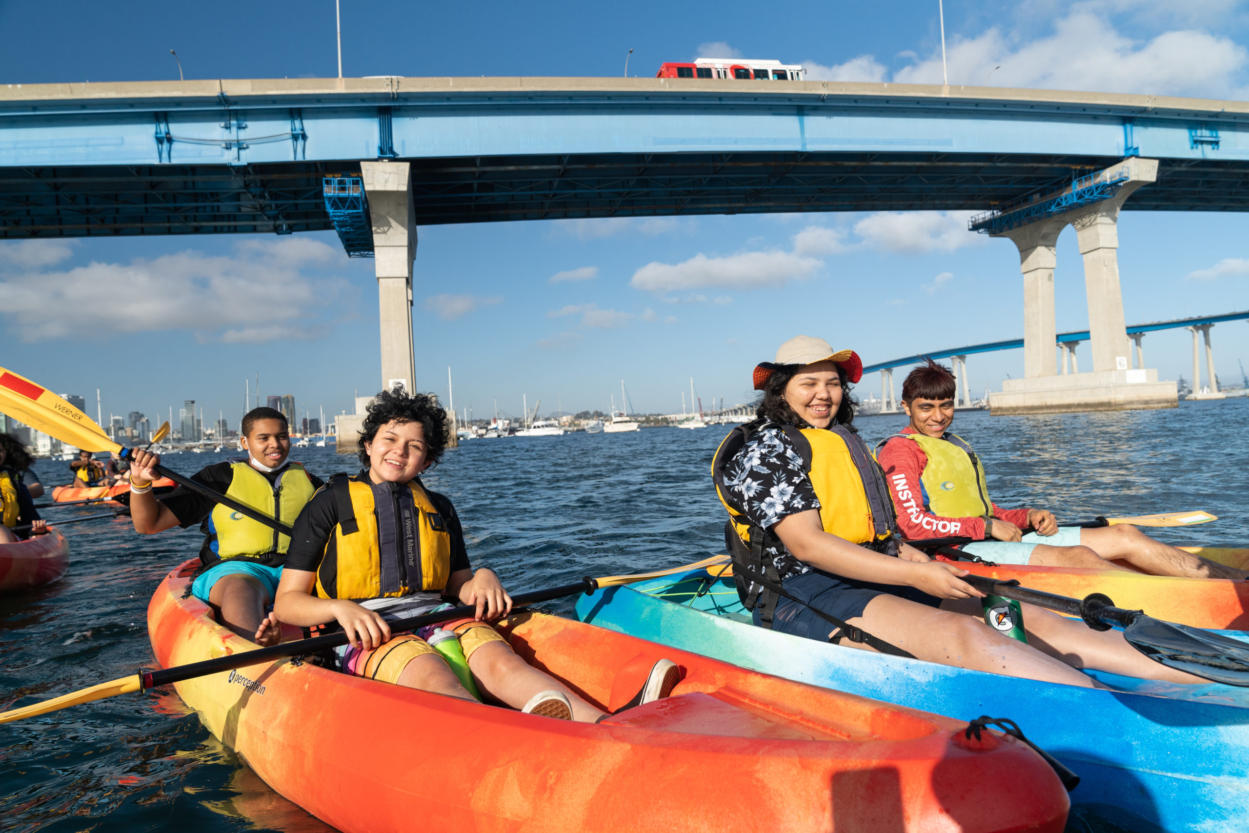 Four Outdoor Outreach youth participants sitting in blue and orange kayaks in the San Diego Bay. 