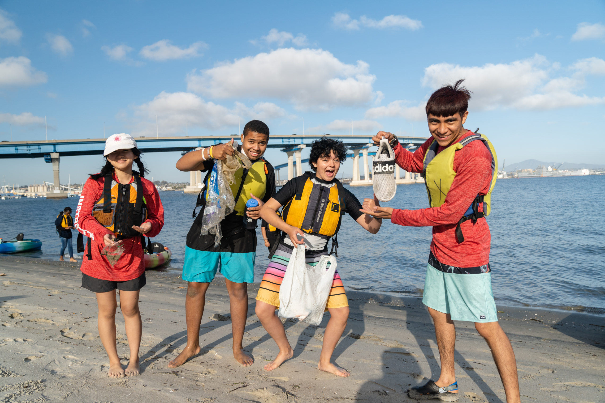 Four Outdoor Outreach youth participants posing on the beach of Tidelands Park and holding up a shoe while smiling.