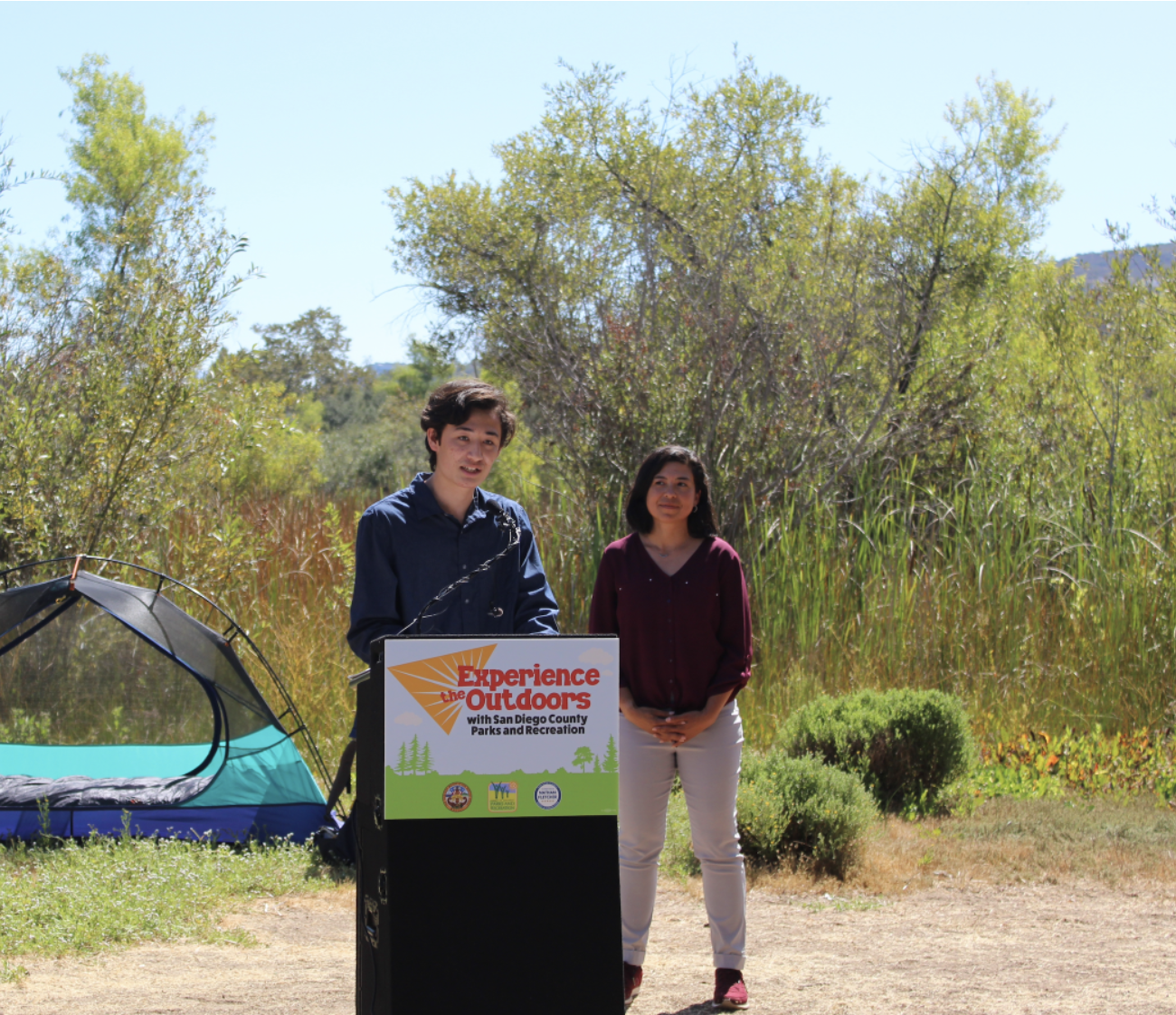 Keanu looking serious as he stands behind a podium while delivering a speech at the County of San Diego's launch of the "Experience the Outdoors" initiative.